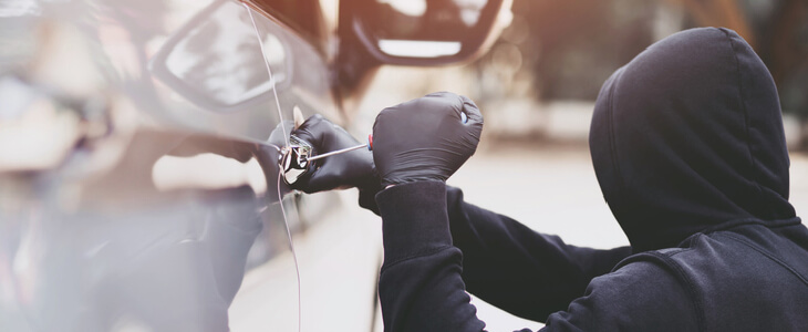 Man wearing black hooded sweatshirt and black gloves attempting to break into a vehicle