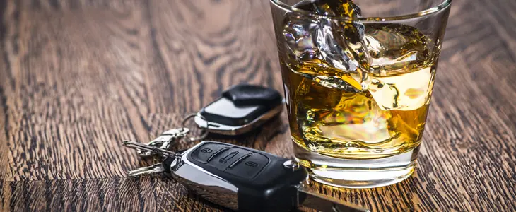 Wooden table with a glass of liquor and a set of car keys next to it
