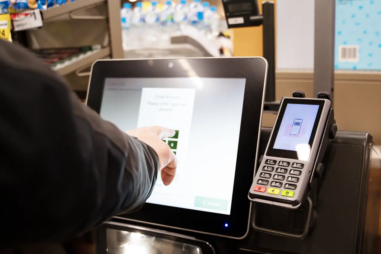 Customer using a self-checkout kiosk by entering an amount on a touchscreen with a card reader beside it.